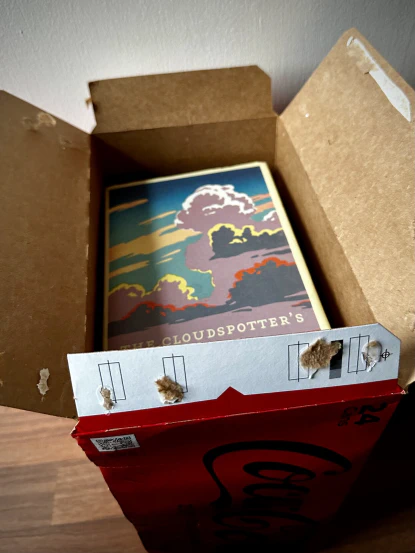 ‘The Cloudspotters Guide’ is peeking, perfectly fitting, from the top of a stack of books packed into a soft drink carton.