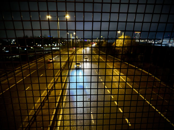 Bright headlights in darkness seen from a rail bridge.