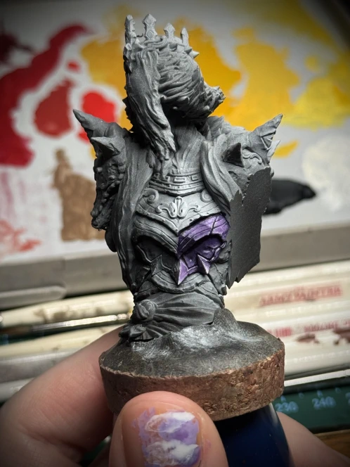 A spooky lady, zenithal primed to highlight light volumes. One of the armour panels is being painted in various shades of purple, the stark changes of contrast aiming for a non-metallic-metal effect.