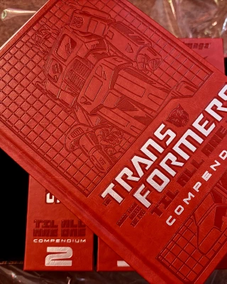 A shot showing the embossed all-red-with-white-text cover of the hardcover, volume 1 sitting on top of volumes 2-4. This is the ‘Autobot’ edition, because I am a good boy.