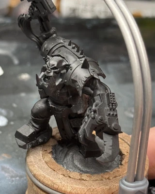 The Mini is an Ork with one big metal hand and one little metal hand. He’s holding a gun that seems to have the same hairstyle as the dwarf I was painting previously. A 
cartoonishly-large eventually-metal jawbone obscures half his face.