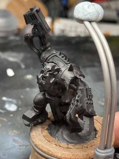 The Mini is an Ork with one big metal hand and one little metal hand. He’s holding a gun that seems to have the same hairstyle as the dwarf I was painting previously. A 
cartoonishly-large eventually-metal jawbone obscures half his face.