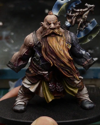 The first full body shot of Not Gotrek that we’ve seen in a while. His hair has been (temporarily) removed so that the reverse of the axe can be tacked to the wrong shoulder and viewed in comparison with the rest of the painting. Some initial reflections have been added to the tiny pieces of shiny chest armour actually visible beneath his massive beard. Eventually the two styles should hopefully match and unify the appearance a little.

Ignore the very WIP badly drawn doggo heads on his arm please. Those aren’t for you.