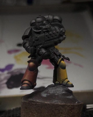 A black-primed Marine mini pictured against a wet palette of purples, yellows and pinks. The boots, shins and kneepads are coloured ‘yellow’ (stage right) and ‘red’ (stage left) in different combinations of that same paint set.