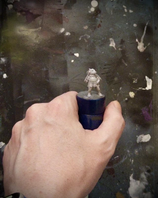 One (1) hand of approximately human proportions holding a tiny horned doggo, placed on a standard-reference painting handle. The doggo is entirely wee. It wears a cool skirt.